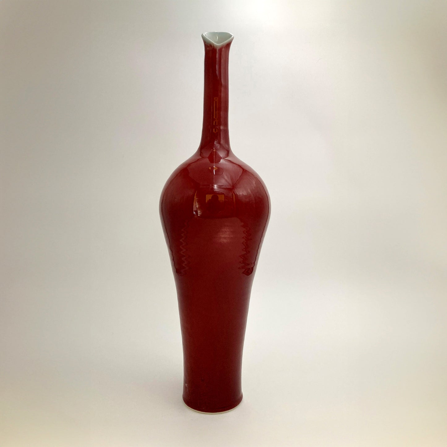 Tall red ceramic vase celadon interior petal rim on a white background