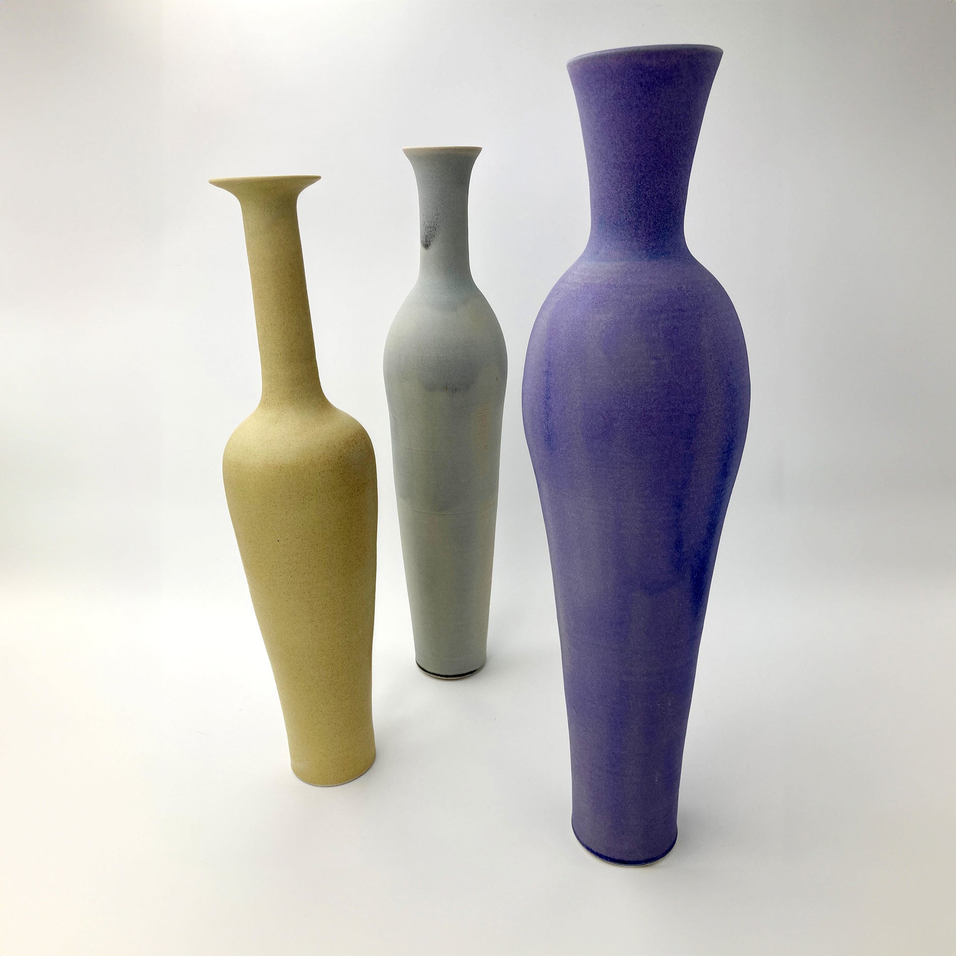 Three tall vases in golden ochre, celadon, and purple on a white background