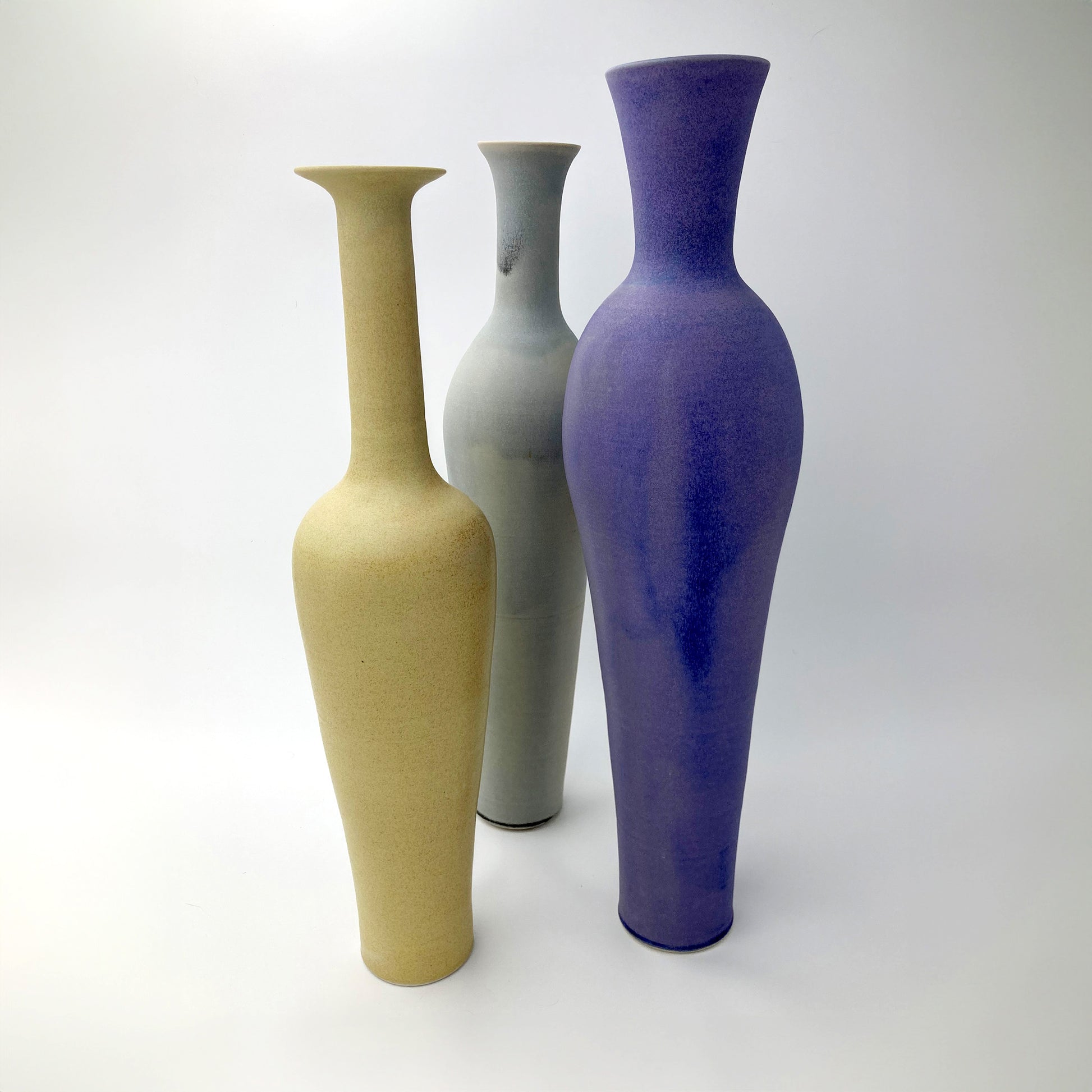 Set of three tall ceramic vases in beige, gray, and purple on a white background